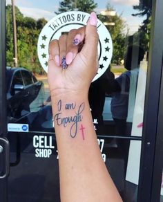 a woman's arm with a tattoo saying i am enough and a cross on it