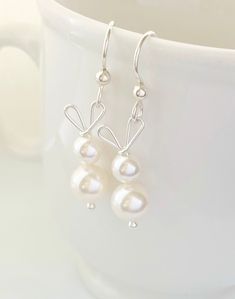 two white pearls are hanging from silver hooks on a mug with a coffee cup in the background