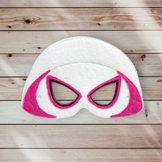 a white mask with pink eyes on top of a wooden table next to a piece of wood