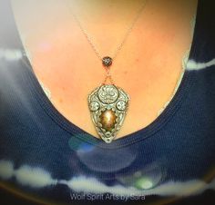 This beautiful shield-style talisman merges the beauties of Elven and Celtic design. This piece showcases a gorgeous and flashy Purple Sunset Labradorite stone! The design also features recessed and flowy filigree details upon a raised circular element; there's also a flower design which could also double as a Celtic cross-like detail! It also has a decorative bail! It's been highlighted with pearl pigment to give it a shiny metal feel, darker pigments for an oxidized look, and it's been sealed Fantasy Polymer Clay Jewelry As A Gift, Silver Polymer Clay Pendant Jewelry, Handmade Polymer Clay Jewelry In Fantasy Style, Handmade Silver Polymer Clay Jewelry, Bohemian Polymer Clay Pendant Jewelry, Mystical Carved Jewelry Gift, Handmade Polymer Clay Jewelry For Collectors, Elven Shield, Sunset Labradorite