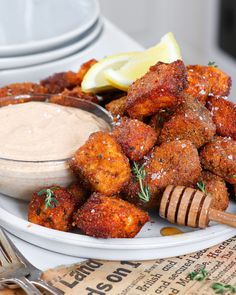 a white plate topped with fried food next to a bowl of dip and a fork