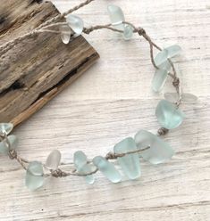 a necklace with sea glass pieces on a wooden board next to a piece of driftwood