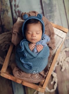 a newborn baby wrapped in a blue blanket and wearing a bear hat is laying on a wooden crate