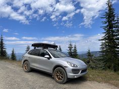 a car parked on the side of a dirt road with trees and mountains in the background