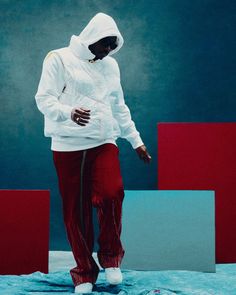 a woman in white hoodie and red pants standing on blue surface with blocks behind her