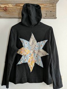 This is a women's black zip-up hooded sweatshirt. There is no size but looks to be L/XL. There is a vintage quilt block on the back. I added pieces of vintage fabric to the front pockets and hand stitched then on. Fraying will happen and is meant to happen.  Measurements- Chest: 20.5 inches Sleeves: 21 inches Shoulder to hem: 22 inches This is a previously owned garment. I search out clothing that looks to be in great condition. I will replace buttons and make repairs as needed. Many of my designs are more rugged and a few rips add to what I want in a look. All clothing should be in a condition to be worn for many years. I wash everything once I bring it home and then I do my creative thing. Buying clothing in this manner saves water and energy. Black Hooded Sweatshirt, Quilted Clothes, Womens Hoodies, Womens Sweatshirts Hoods, Sweatshirt Women, Vintage Quilt, Sweatshirt Vintage, Black Zip Ups, Vintage Quilts