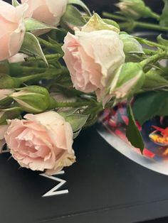 some pink roses are sitting on a table next to a plate with the word mom written on it