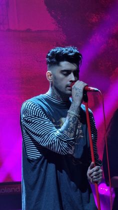 a man with tattoos on his arm holding a microphone in front of a purple background