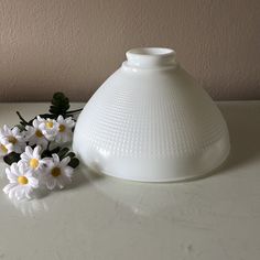 a white vase sitting on top of a table next to some daisies in front of it