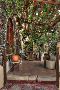 an outdoor patio with potted plants on the side and stone walls, along with a pergolated roof