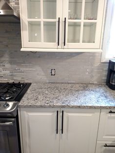 a kitchen with white cabinets and granite counter tops in front of a black stove top oven