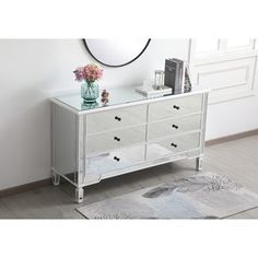 a white dresser with drawers and flowers on top in a room next to a mirror