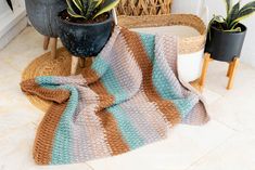 a crocheted blanket sitting on top of a floor next to potted plants