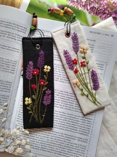 two bookmarks with flowers on them sitting next to an open book and some beads