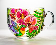 a colorful glass cup with flowers painted on it's side and hummingbird in the middle