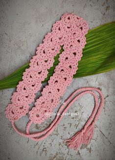 a pink crocheted scarf laying on top of a green leaf next to a tassel