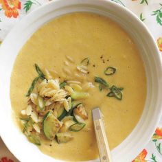 a white bowl filled with soup on top of a floral table cloth next to a wooden spoon