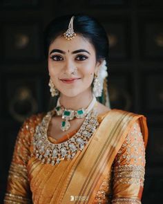 a woman in an orange and gold sari with jewelry on her neck, smiling at the camera