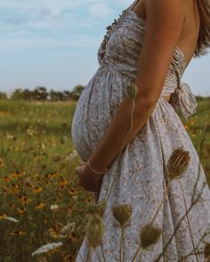 a pregnant woman standing in a field with wildflowers