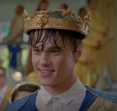 the young man is wearing a crown and smiling at the camera while standing in front of other people