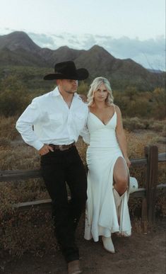 a man in a cowboy hat standing next to a woman wearing a long white dress