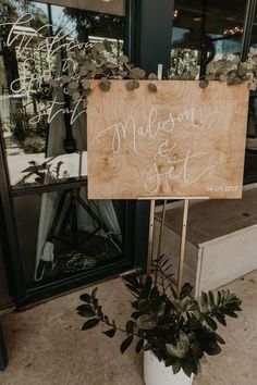 a wooden sign sitting on the side of a building next to a potted plant