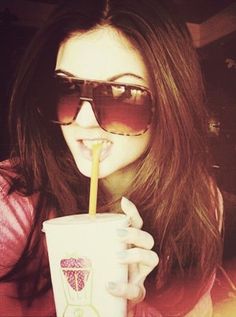 a woman wearing sunglasses and drinking from a paper cup with a straw in her mouth