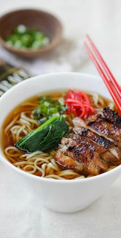 a white bowl filled with noodles and meat next to chopsticks on a table