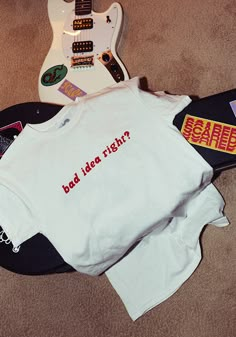 a t - shirt that says bad idea right next to an electric guitar on the floor