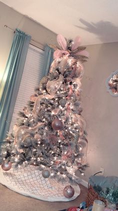 a decorated christmas tree in a living room with blue curtains and pink ornaments on it