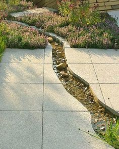 a garden with rocks and water running through the center, surrounded by green grass and purple flowers