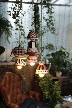 several lamps hanging from the ceiling in a room with chairs and potted plants behind them