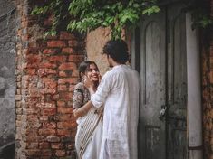 two people standing next to each other in front of a brick building