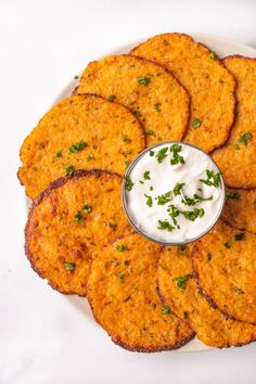 a white plate topped with potato patties covered in ranch sauce and garnished with parsley