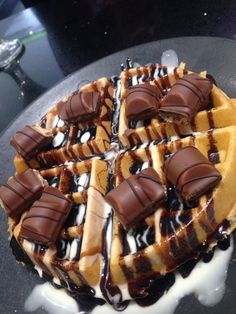 a waffle topped with chocolate and drizzled in white sauce on a black plate