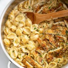 a pot full of chicken and pasta with a wooden spoon