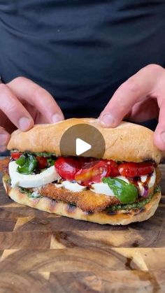 a person holding a sandwich on top of a wooden cutting board