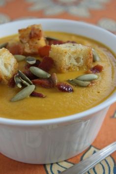 a white bowl filled with soup and croutons on top of an orange table cloth