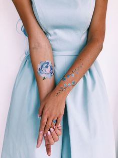 a woman in a blue dress holding her hands with tattoos on it's arms