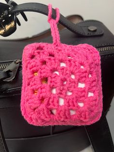 a pink crocheted square hanging from a black bag