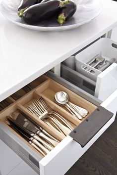 an open drawer with utensils and silverware in it on a white table