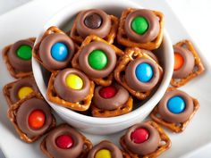 a white bowl filled with candy covered pretzels on top of a white plate