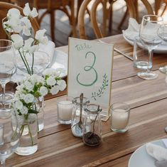 the table is set with white flowers, candles and place cards for guests to sit at