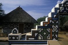 an artisticly designed bench in front of a thatched roof hut with geometric designs on it