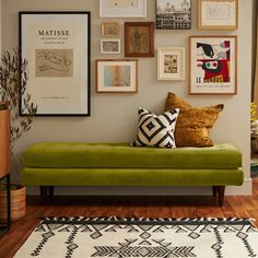 a green couch sitting in front of a wall filled with pictures and framed art on it