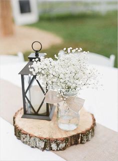 a vase filled with white flowers sitting on top of a wooden table next to a lantern