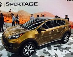 a gold colored car is on display at an auto show with people standing around it