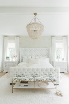 a white bedroom with a chandelier hanging from the ceiling and an upholstered bed