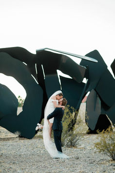 a bride and groom standing in front of a large piece of art that looks like a sculpture