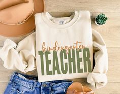 ** ORDER CUT-OFF DATE FOR CHRISTMAS DELIVERY IS DECEMBER 9TH. 2024 ** Cozy up this fall in our stylish kindergarten teacher sweatshirt, perfect for educators who want to show off their passion in a chic way. The word 'TEACHER' stands out in bold, eye-catching letters, while 'kindergarten' is elegantly displayed in a delicate script font, artistically cut out at the top of the word for a unique layered effect. This fall kindergarten teacher sweatshirt is perfect for crisp fall days in the classro Teacher First Day Of School, Gifts For Teacher, Mrs Sweatshirt, Team Sweatshirts, Funny Teacher Gifts, Teacher Team, Teacher Sweatshirt, First Grade Teachers, Funny Teacher